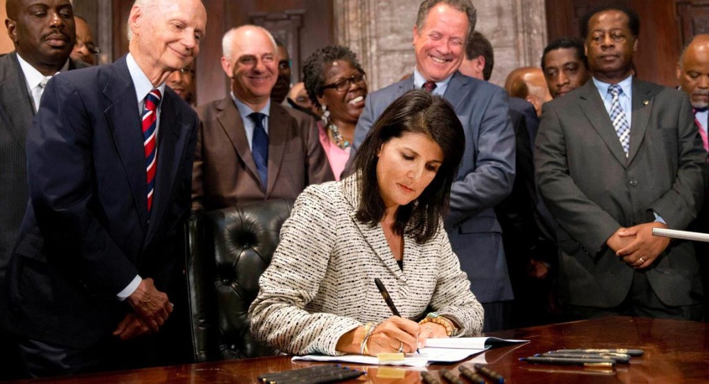 South Carolina Gov. Nikki Haley signs a bill into law as former South Carolina governors and officials look on Thursday, July 9, 2015, at the Statehouse in Columbia, S.C. The law enables the removal of the Confederate flag from the Statehouse grounds more than 50 years after the rebel banner was raised to protest the civil rights movement. (AP Photo/John Bazemore)